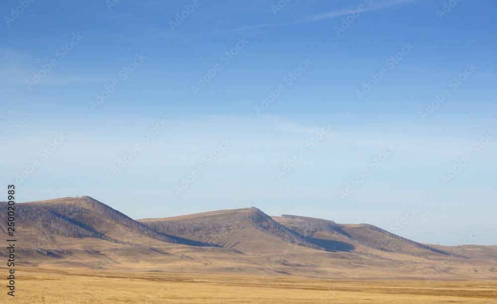 Smooth hills covered with dry grass on horizon with blue sky in Khakassia, Russia