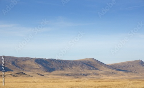 Smooth hills covered with dry grass on horizon with blue sky in Khakassia  Russia