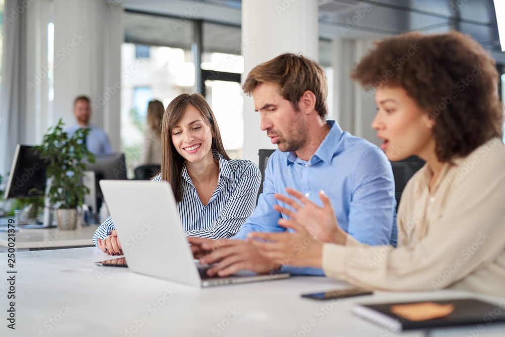 Coworkers sitting at table and solving problem. Man using laptop while two female colleagues looking at laptop and helping him.. Coworkers sitting at table and solving problem. Man using laptop while two female colleagues looking at laptop and helping him..