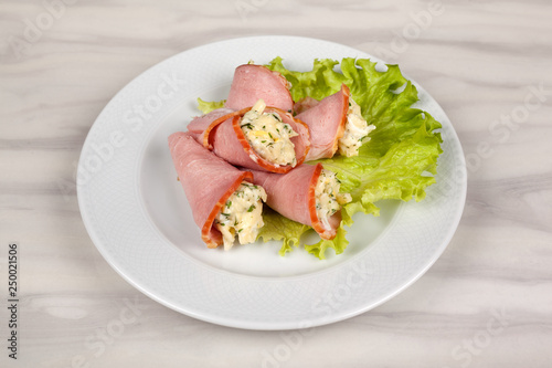 Ham roll stuffed with cheese and green salad on a white plate.