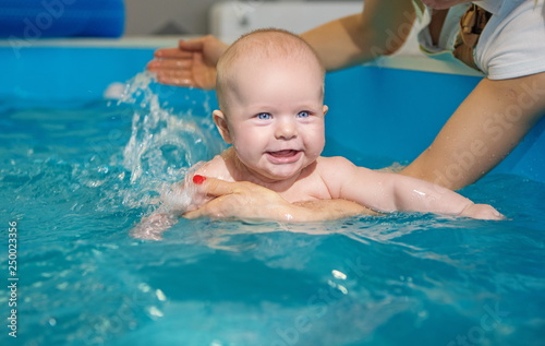 Baby in pool bathing health procedures with mother hands swimming