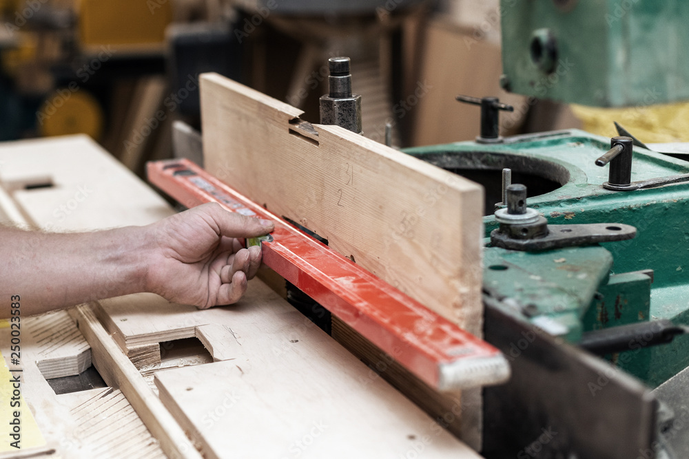 High quality wood concept. Cropped photo of cabinetmaker handcraft tradesman hold red surf level in hands check correct position of the wood High quality wood concept. Cropped photo of cabinetmaker handcraft tradesman hold red surf level in hands check correct position of the wood