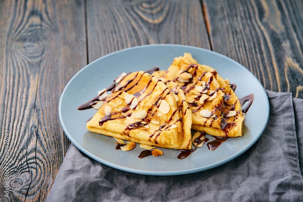 Two pancakes with chocolate syrup, almond flakes on plate, honey flows from spoon, side view Two pancakes with chocolate syrup, almond flakes on plate, honey flows from spoon, side view