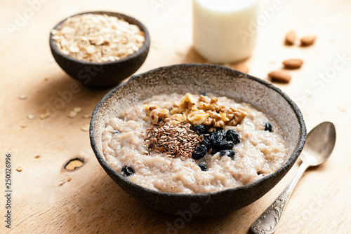 Oatmeal porridge with raisin and seeds in bowl on wooden table. Tasty healthy breakfast. Morning vegan meal