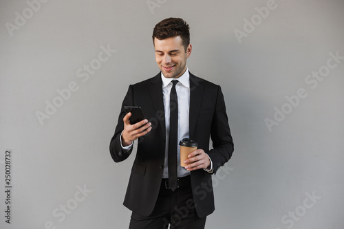 Handsome young businessman walking outdoors at the street using mobile phone.