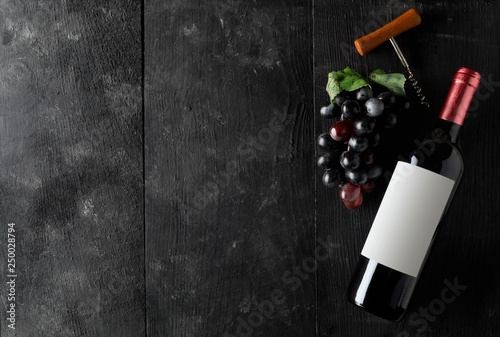 Red wine bottle with corkscrew and grapes on dark wooden table flat lay from above