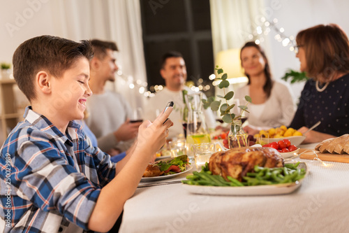 technology, holidays and people concept - happy boy with smartphone having family dinner party at home