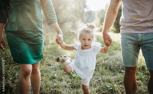 A midsection of young family with a small daughter walking in sunny summer nature.