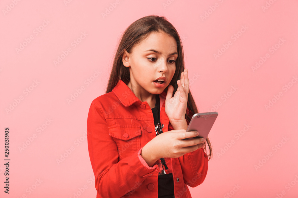 Image of surprised teen girl in casual using smartphone while standing, isolated over red background Image of surprised teen girl in casual using smartphone while standing, isolated over red background
