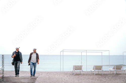 Two men photographer friends with camera and smartphone in hand are walk at the beach during their holidays. work and travel, enjoy the moment, freelancers enjoy life, space for te?t