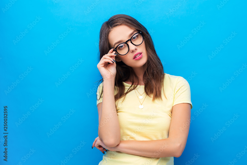 people concept - smiling young woman or teenage girl in yellow t-shirt and glasses over bright blue background people concept - smiling young woman or teenage girl in yellow t-shirt and glasses over bright blue background