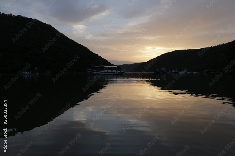 Boats, ships on the Lim Canal, Lim Fjord, Lim Bay. Summer, warm, holiday, evening. Calm, pleasant end of the day. Dusk, twilight, sunset in Croatia. Colorful sky reflecting in the water surface.