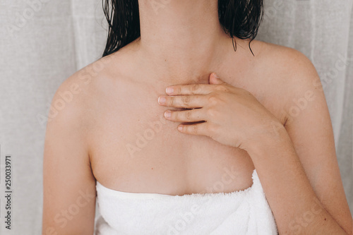 Relaxed sexy woman in white towel applying moisturizing cream on neck in bathroom  closeup. Skin and body care. Slim young woman enjoying spa and wellness.