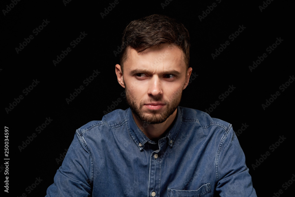 Man in denim shirt looking sideways with doubtful expression Man in denim shirt looking sideways with doubtful expression