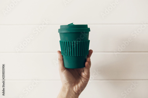 Fotka „ Ban single use plastic. Hand holding stylish reusable eco coffee  cup on white wooden background. Green Cup from natural bamboo fiber, zero  waste concept. Make a choice. Take away coffee“ ze