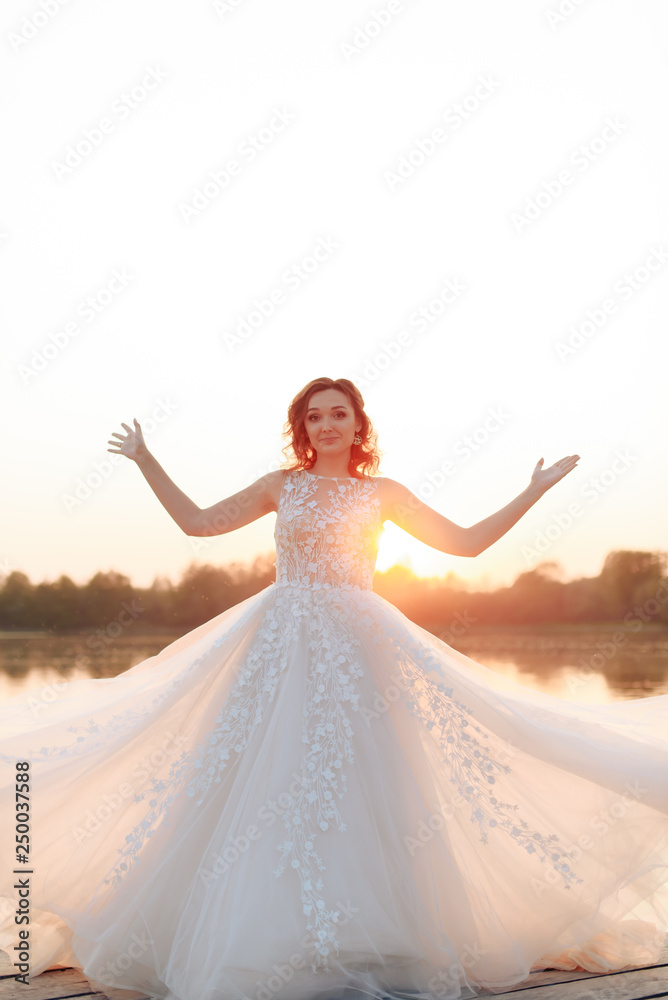young beautiful bride in white dress on wooden pier near water at sunset young beautiful bride in white dress on wooden pier near water at sunset
