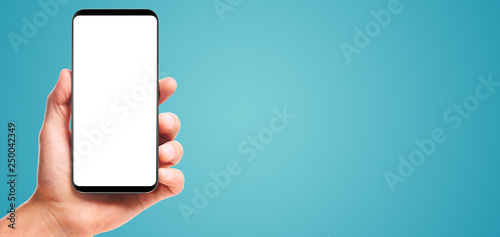 male hand holding bezel-less smartphone with blank screen, isolated on blue background . Screen is cut out with path photo