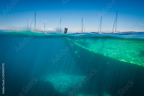 View from water line on old ship wreck and seven sailing boats anchored in close area. Sunny weather and clean water.