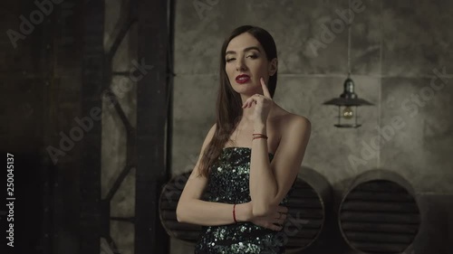 Portrait of provocative fatal brunette female staring with tempting, passionate look while flirting indoors. Stunning vamp woman in cocktail dress looking playful and beckoning, expressing desire.
