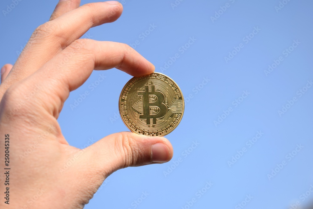 Fototapeta premium Hand holding golden bitcoin coin on blue sky background