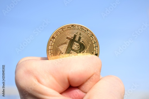 Hand holding golden bitcoin coin on blue sky background photo