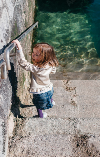 Niña sonriendo alegre mientras baja las escaleras para tocar el agua