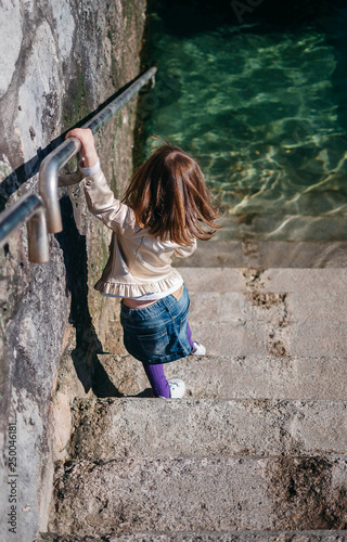 Niña bajando por las escaleras a tocar el agua en un día soleado