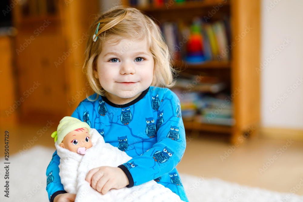 Adorable cute little toddler girl playing with doll. Happy healthy baby child having fun with role game, playing mother at home or nursery. Active daughter with toy. Adorable cute little toddler girl playing with doll. Happy healthy baby child having fun with role game, playing mother at home or nursery. Active daughter with toy.