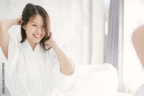 Young Asian woman looking her face in mirror in bathroom