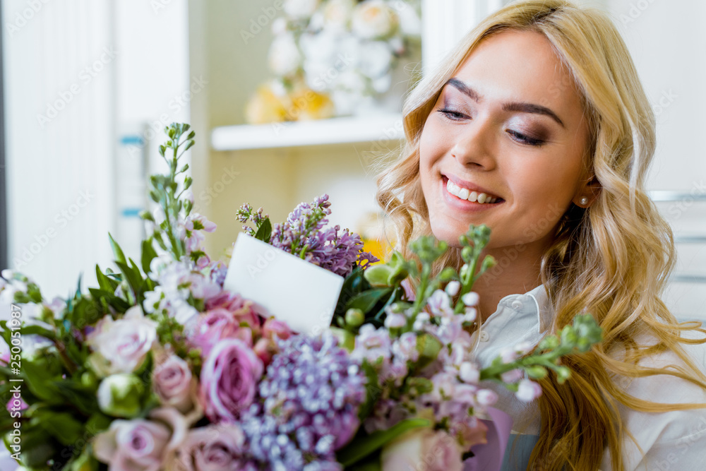 beautiful smiling woman holding flower bouquet with roses, lilac and card with copy space