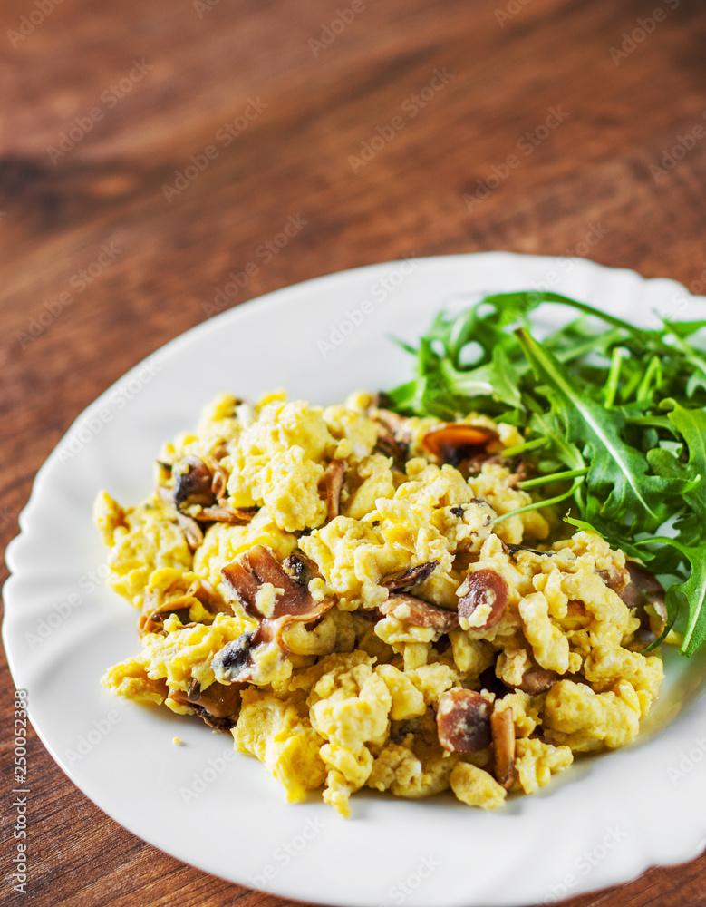 scrambled eggs with mushrooms and arugula salad in white plate on wooden table background