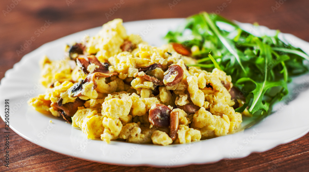 scrambled eggs with mushrooms and arugula salad in white plate on wooden table background scrambled eggs with mushrooms and arugula salad in white plate on wooden table background