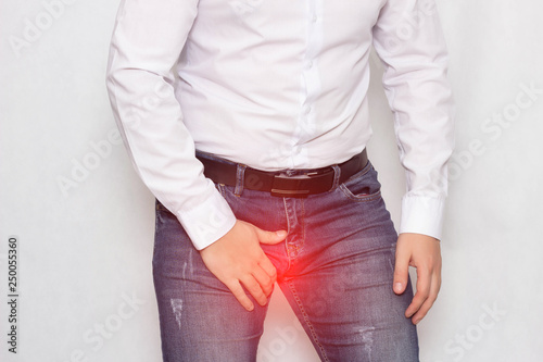 Bild auf Leinwand A man on a white background in a white shirt holding on to his groin he has pain
