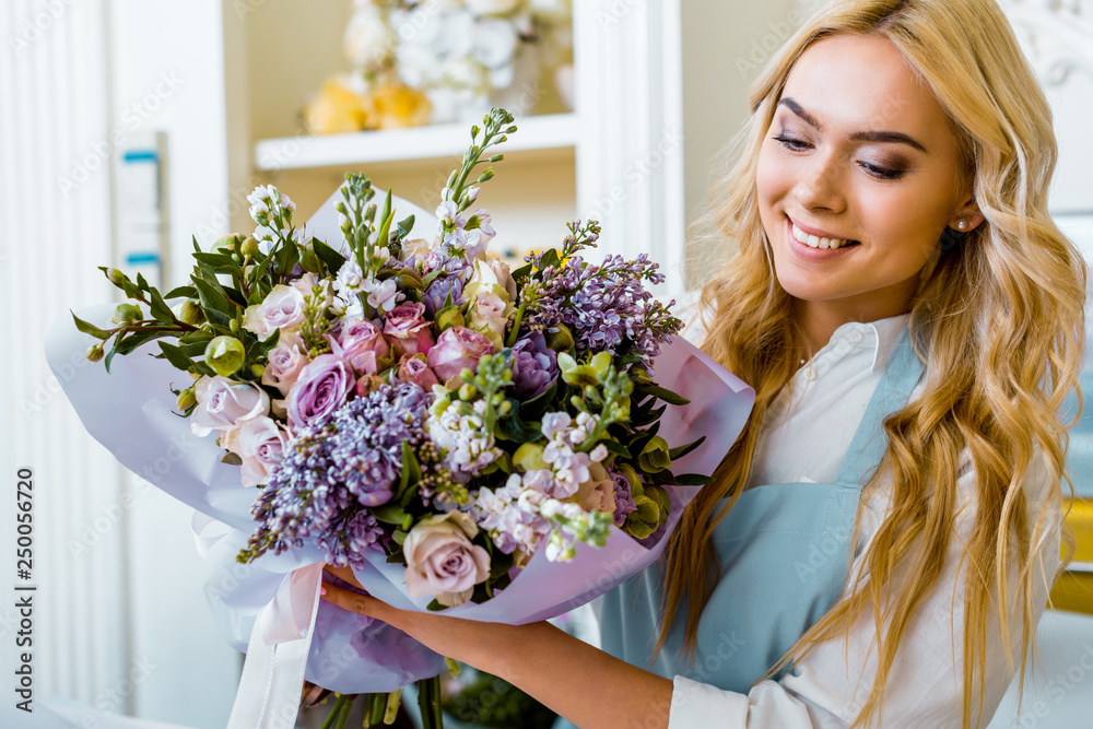 selective focus of beautiful smiling female florist holding bouquet in flower shop selective focus of beautiful smiling female florist holding bouquet in flower shop