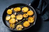 Fried potatoes with garlic and rosemary in a frying pan. Top view, black background.