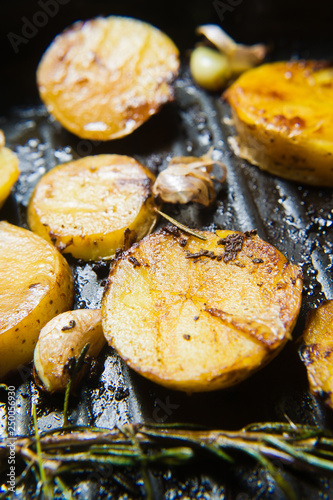 Fried potatoes with garlic and rosemary in a frying pan. Top view, black background, close up.