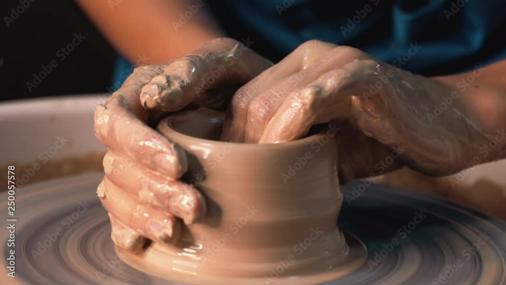 Experienced potter shapes the clay product - jug - with pottery tools. Close up of male hands working on potter's wheel. Shot of half-finished ceramic vase spinning on jigger. 4k.