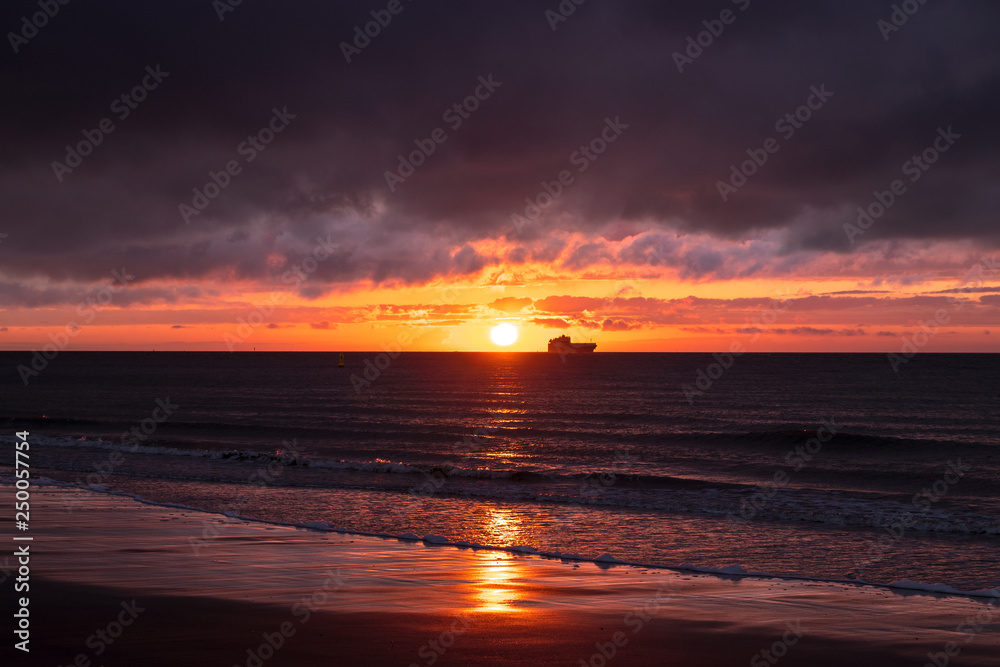 Beautiful colourful sunset over a Dutch beach, ship floating on the horizon
