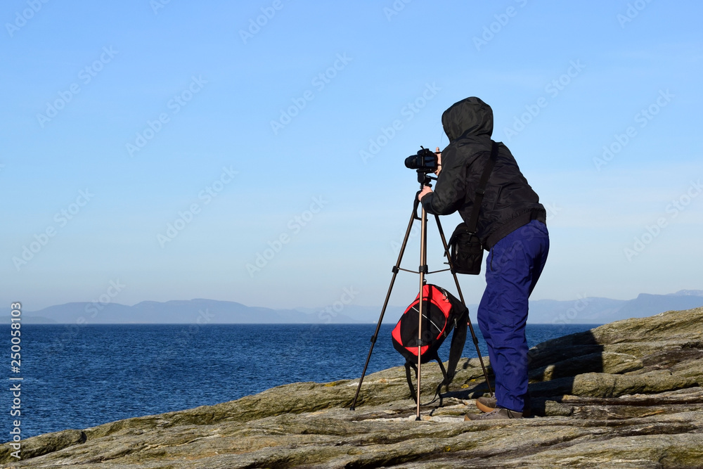 A girl with a camera photographs the sea. Naturalist photographer. Travel to Norway. North Sea.