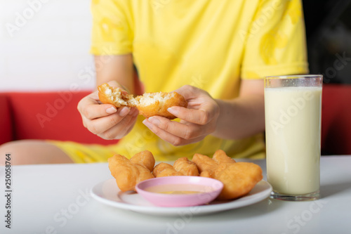 Hand of woman tearing fried buns before eat with the glass of soybean milk on the table