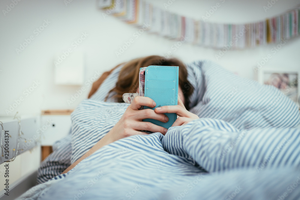 Girl in bed is looking on her smartphone, blurry Girl in bed is looking on her smartphone, blurry