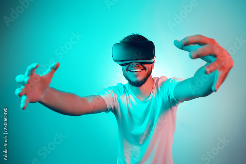Handsome excited bearded man trying VR headset and exploring another world on the colorful background. Smartphone using with VR headset.