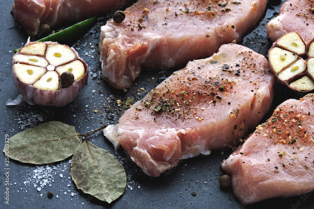 Raw pork steaks with spices before cooking. Appetizing meat on a stone board with spices. The recipe for pork steaks. Raw pork steaks are marinated in seasonings. Raw pork steaks with spices before cooking. Appetizing meat on a stone board with spices. The recipe for pork steaks. Raw pork steaks are marinated in seasonings.