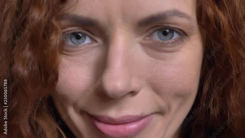 Closeup portrait of adult caucasian female face with red curly hair and beautiful blue eyes looking straight at camera Closeup portrait of adult caucasian female face with red curly hair and beautiful blue eyes looking straight at camera