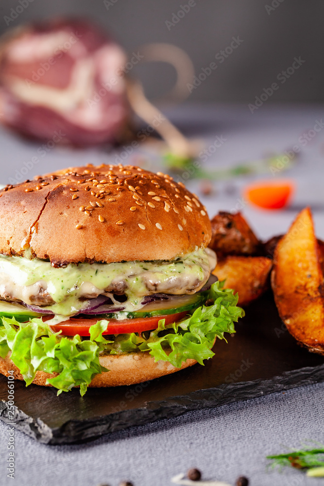 American burger with meat patty, tomato, cucumber, green sauce. Sauce and for french fries on a black stone slate board. Dish in a fast food restaurant. Copy space American burger with meat patty, tomato, cucumber, green sauce. Sauce and for french fries on a black stone slate board. Dish in a fast food restaurant. Copy space
