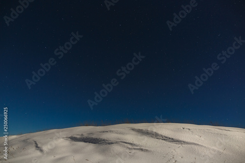 Stars with clouds in the night sky over a snowy mountain ridge. The background of deep space is photographed under the full moon.