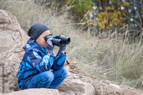 boy sitting on a stone and watching through binoculars