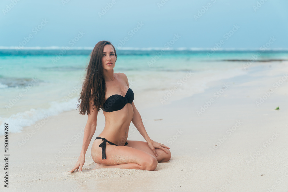 Sexy brunette girl in a swimsuit sunbathes on the white sand beach. Sexy brunette girl in a swimsuit sunbathes on the white sand beach.