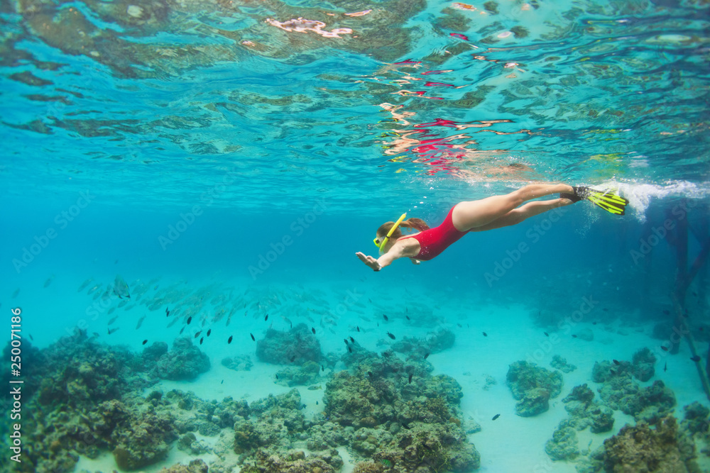 Young happy girl in snorkeling mask jump and dive underwater to see tropical fishes in coral reef sea pool. Travel activity, water sports, outdoor adventure, on family summer beach holiday with kids