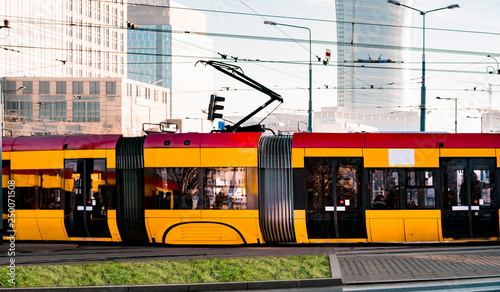 Yellow and red public tram moves in downtown of the big city with modern skyscrapers on background. Urban transportation. Bendy bit of a bendy tram